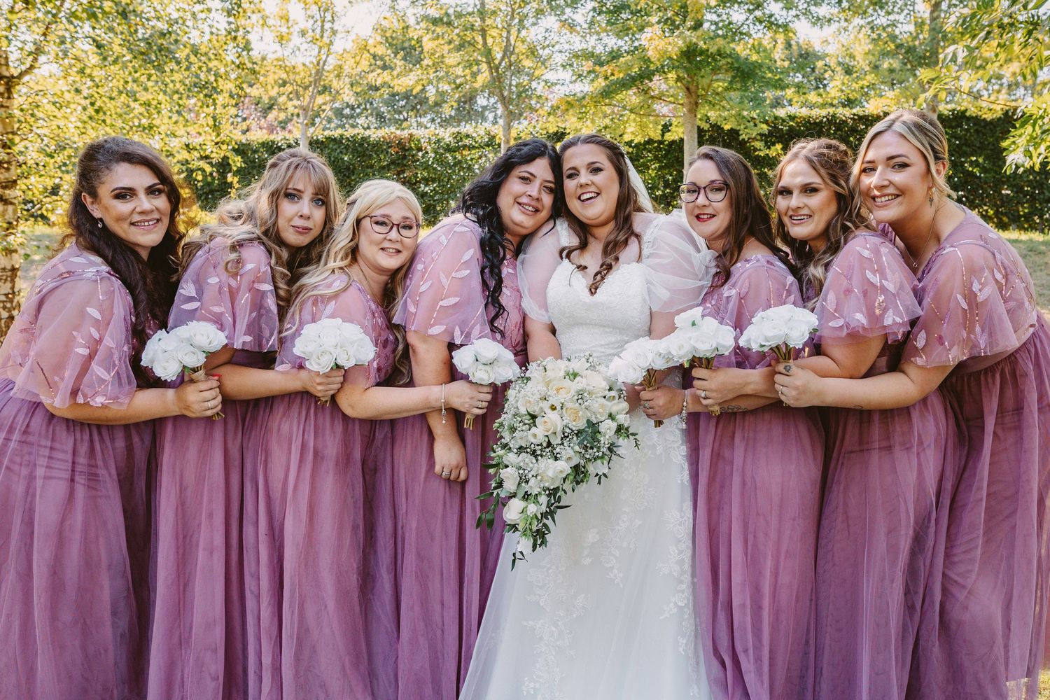 Bride with bridesmaids cuddling into her bridesmaids wearing orchard pink