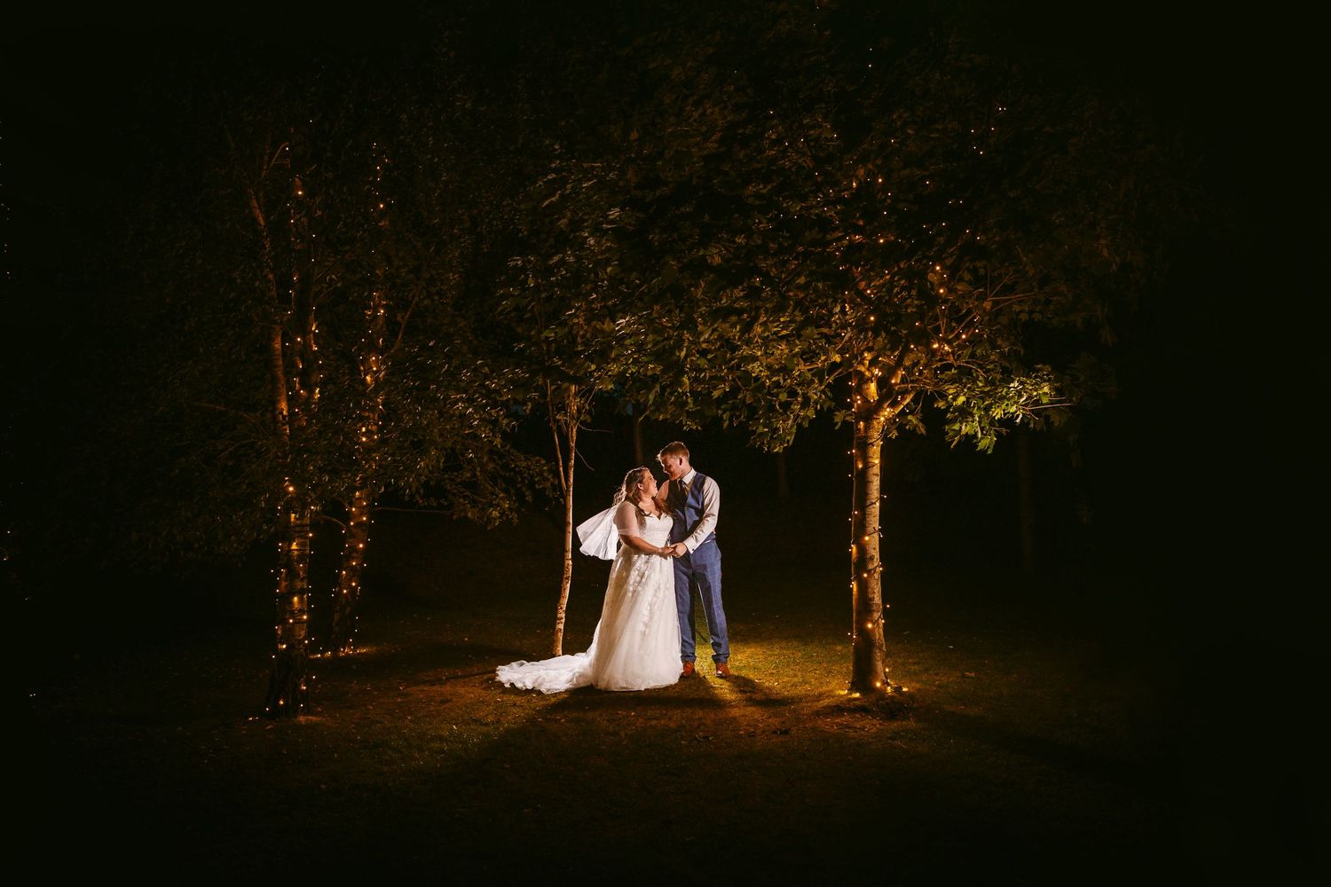 Bride and Groom Portrait in garden at night with pretty lights in trees Stone Barn The Cotswolds