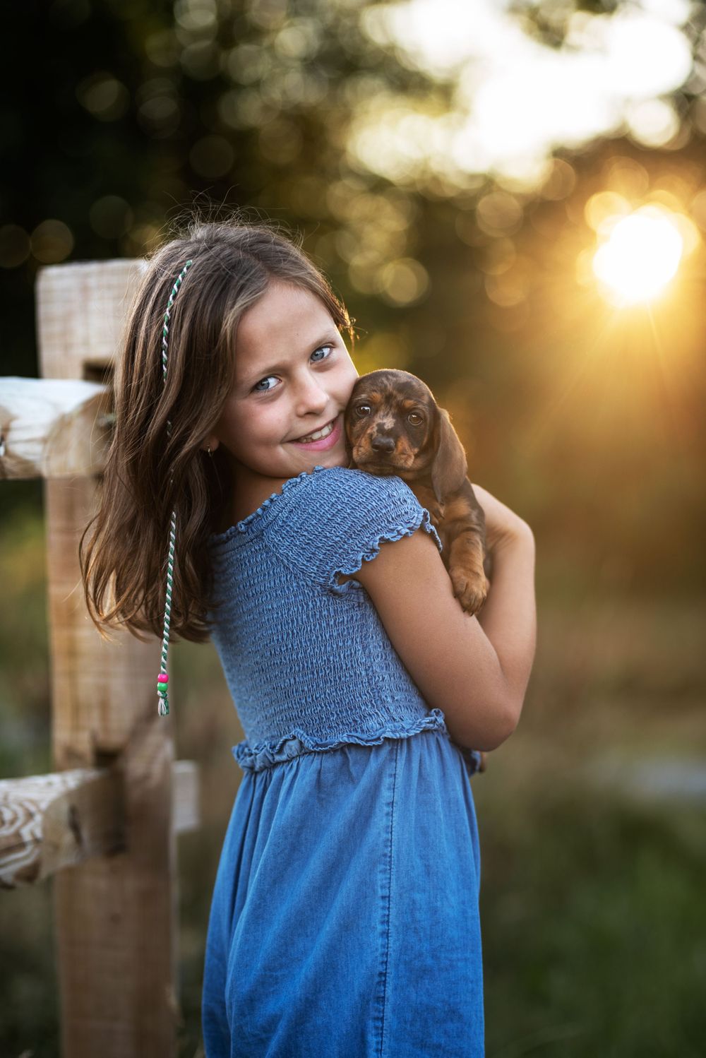 Young person in blue dress holding small dachshund puppy at sunset.