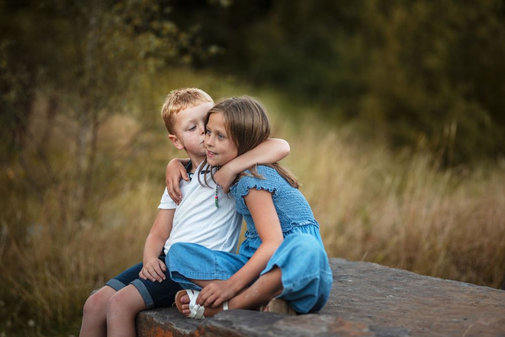 Figures embracing on a rustic wooden bench in a meadow at sunset.
