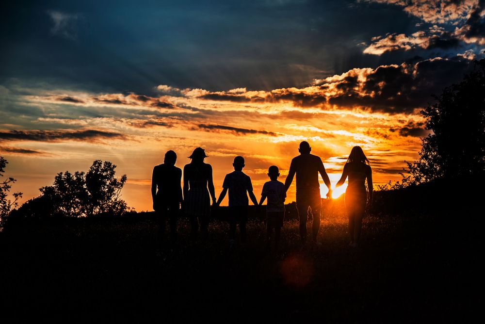 Panoramic silhouette of people gathered together against a dramatic orange sunset sky.