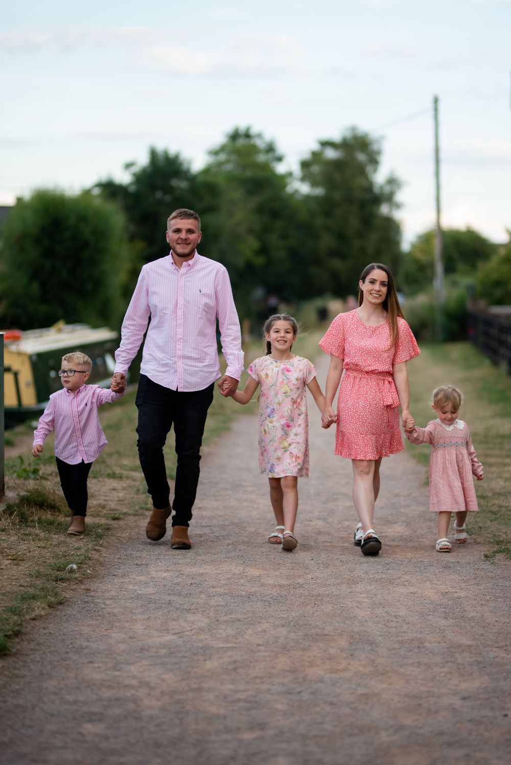 Family walking together down a dirt path wearing coordinated pink and coral outfits.