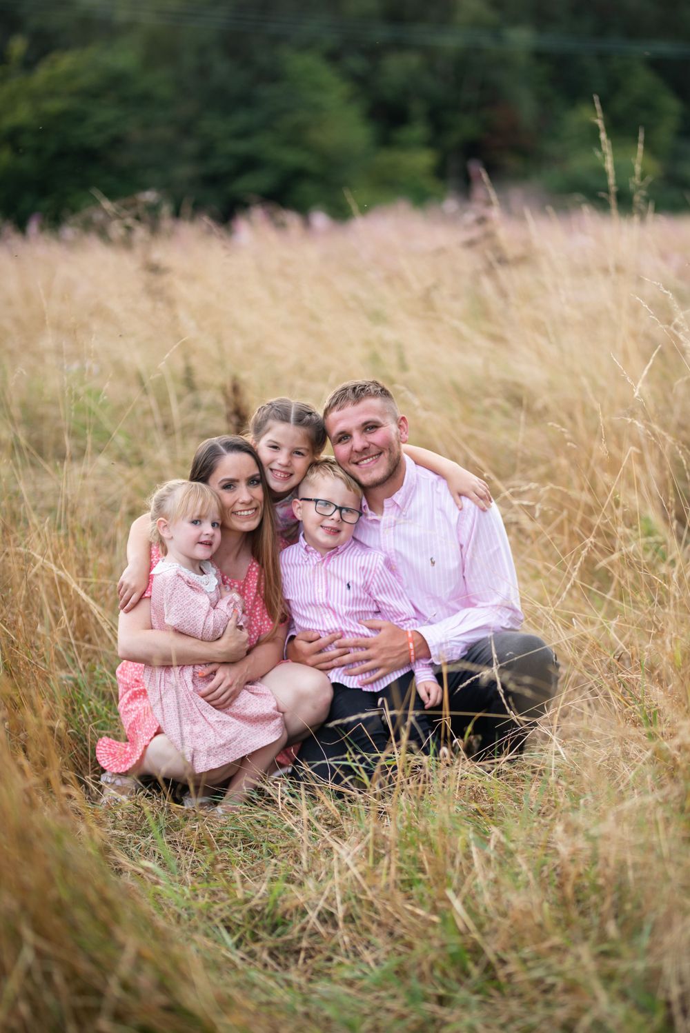 Family group relaxing together in tall summer grass wearing coordinated pink outfits.