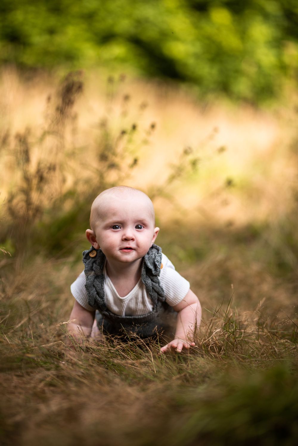 Baby crawling on grass in white outfit with soft focus natural background.
