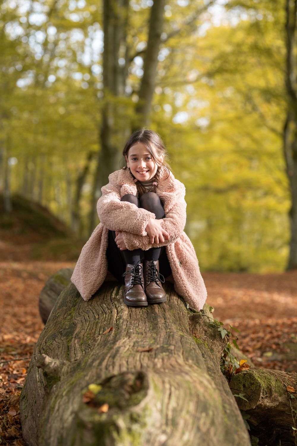 Person in fluffy pink sweater sitting on large fallen tree trunk in autumn forest.