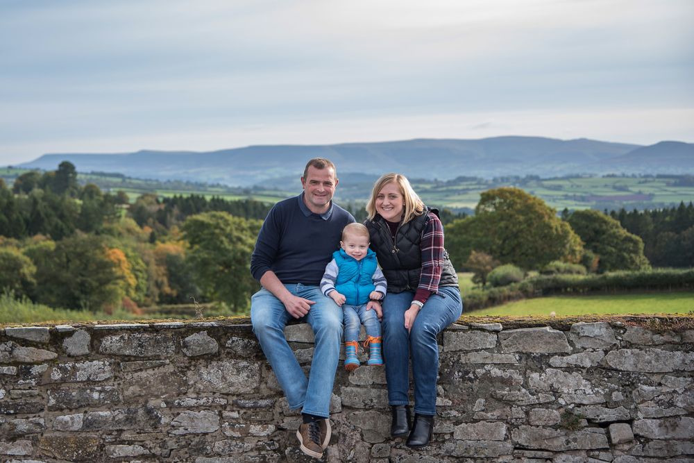 Family gathering on an ancient stone wall overlooking rolling countryside hills at sunset.