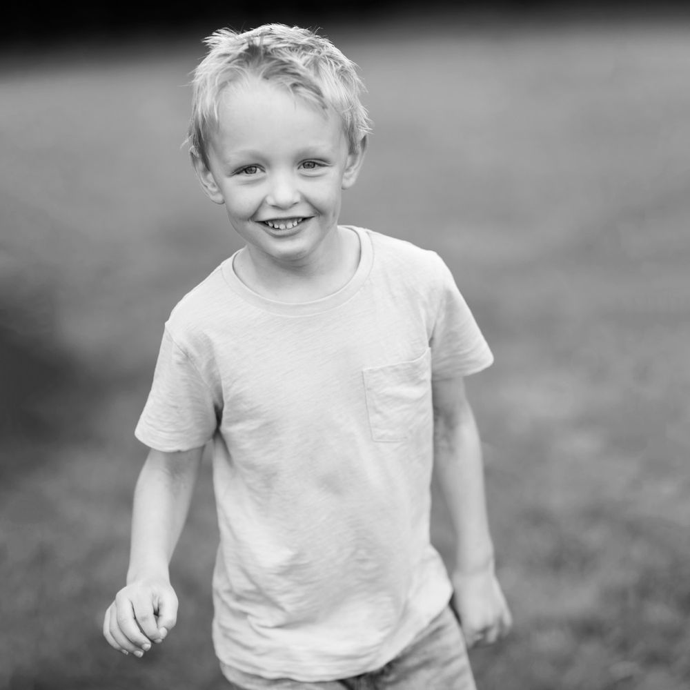Black and white portrait of a young child in a white t-shirt outdoors.