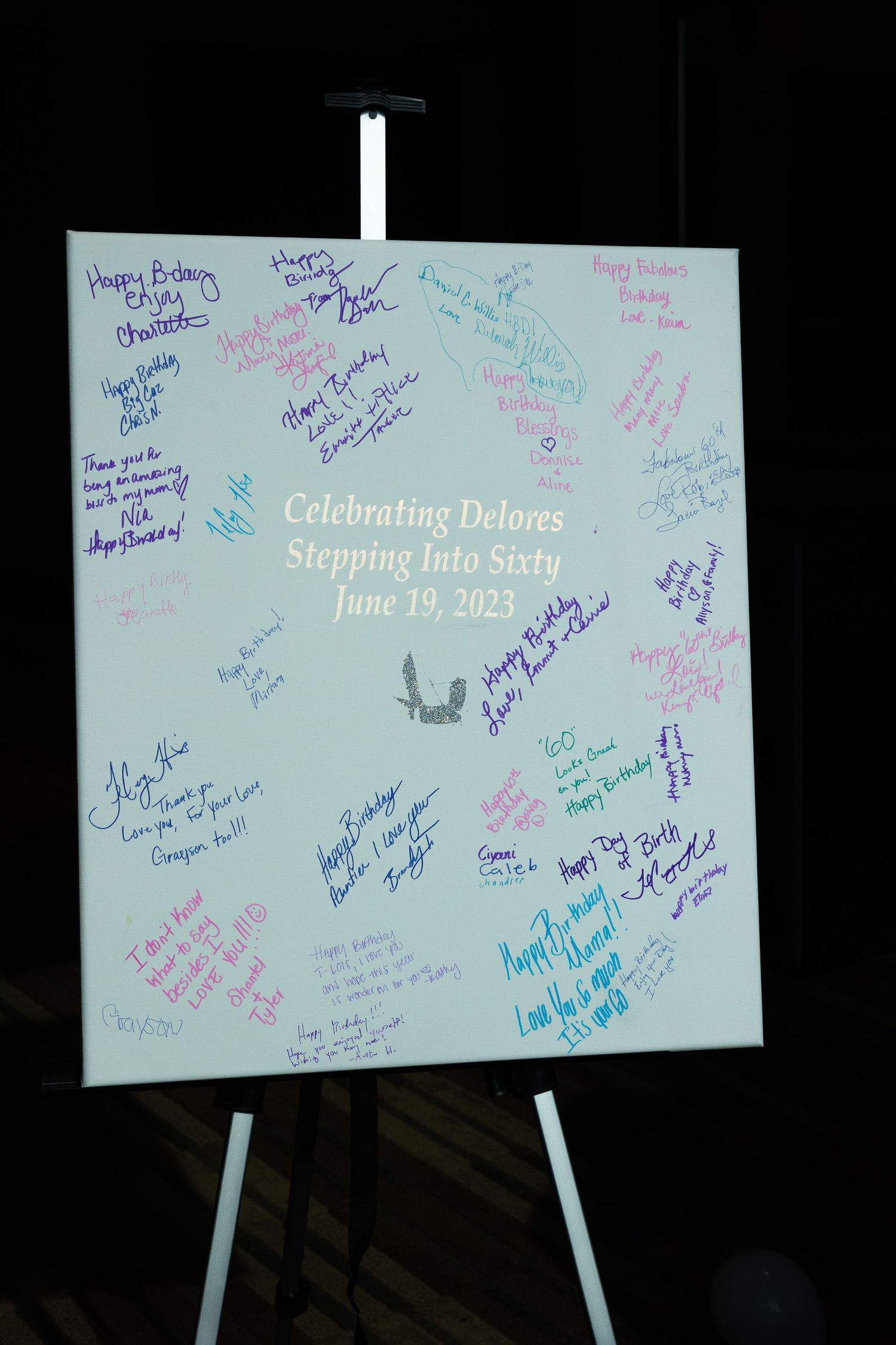 White celebration sign board covered in colorful birthday messages and signatures.