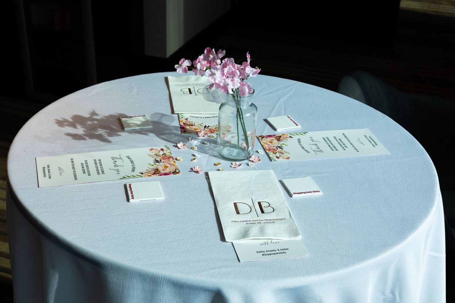 Table settings with cards and pink floral decorations on white tablecloth.