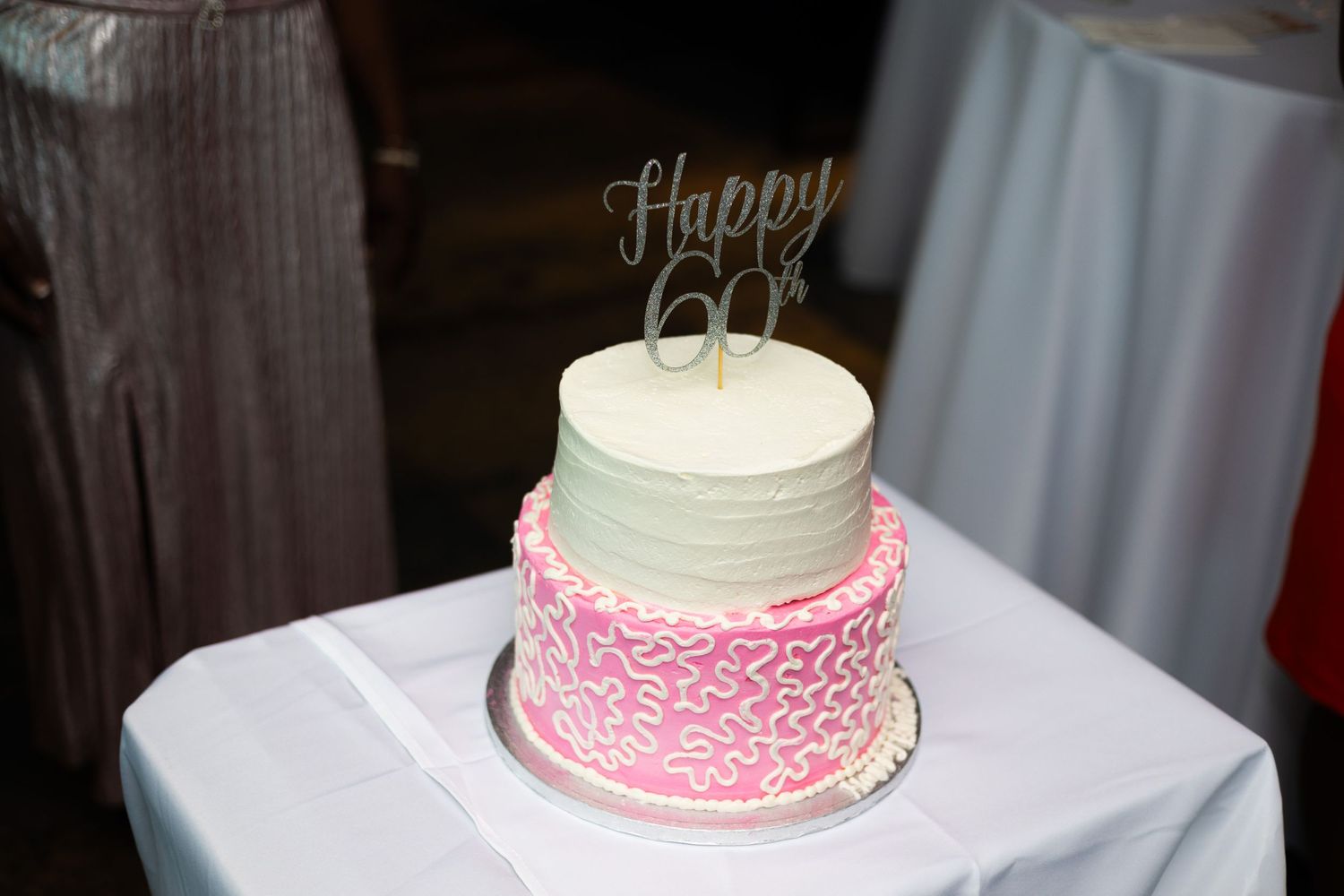 White and pink two-tier birthday cake with 'Happy 60' topper on display.