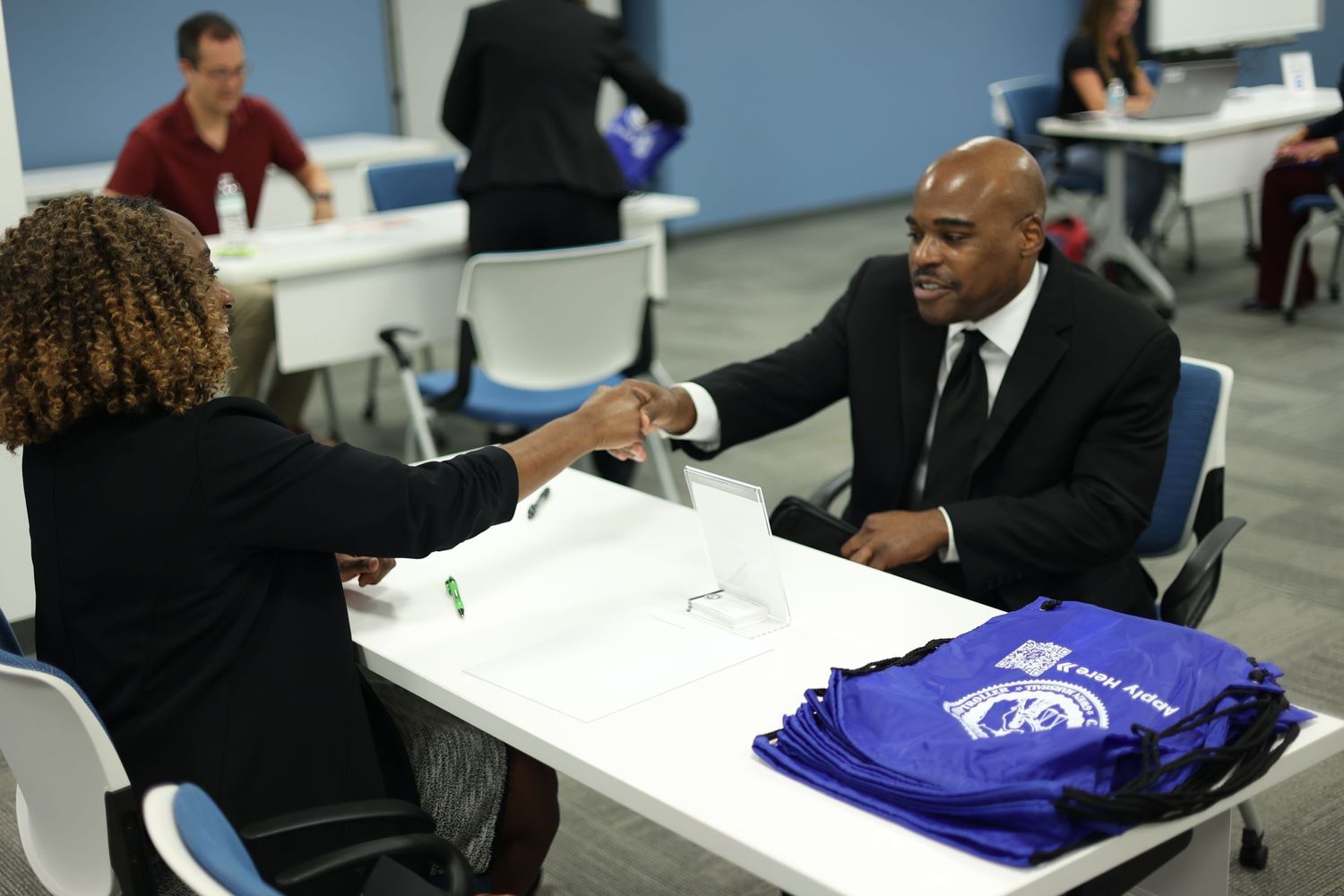 Career fair scene with staff distributing blue uniforms at registration table.
