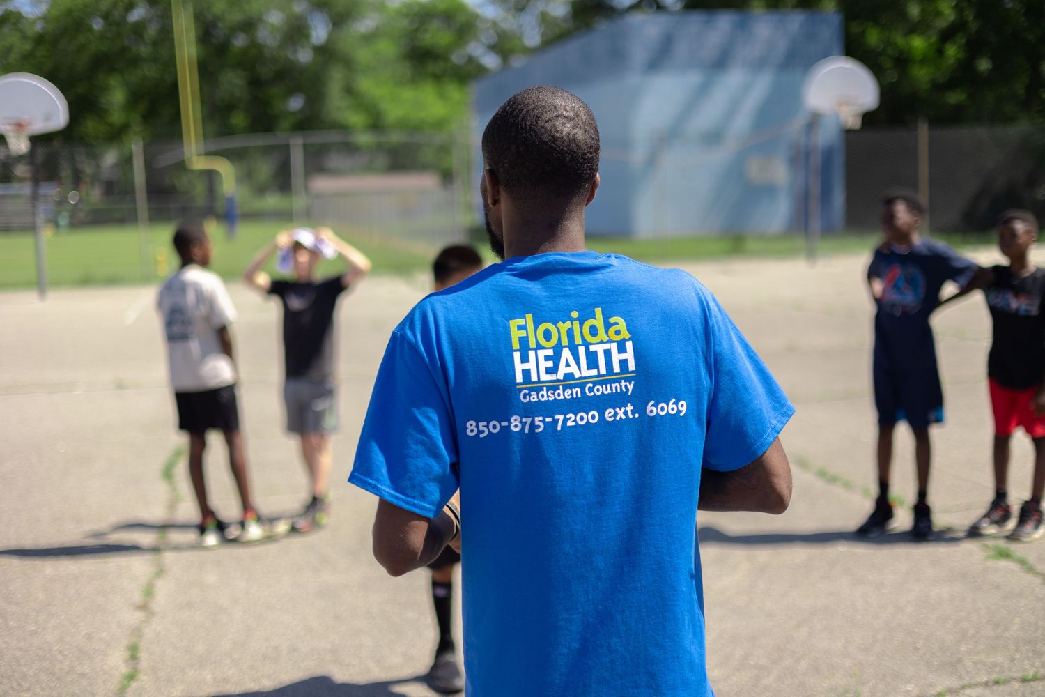 Florida Health staff member supervising sports activities on a sunny outdoor court.