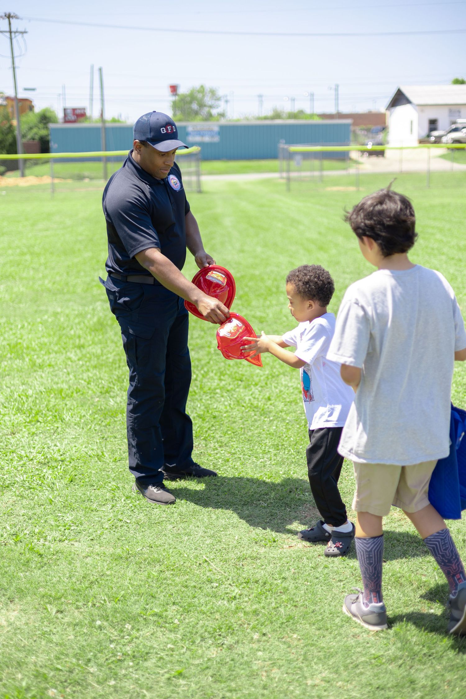 Adult sharing sports equipment with children on a sunny grass field.