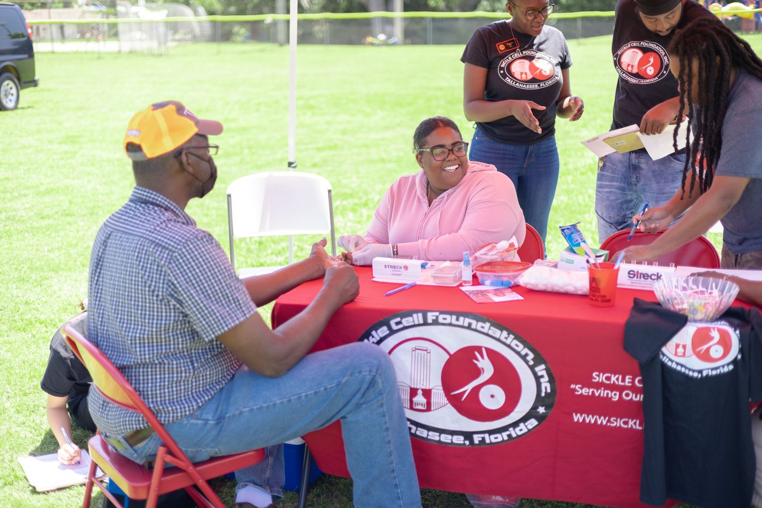 People seated at a red-themed information booth table outdoors.