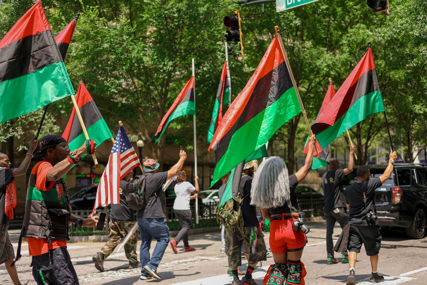 A crowd marches with red, black and green Pan-African flags while carrying signs at a protest rally.