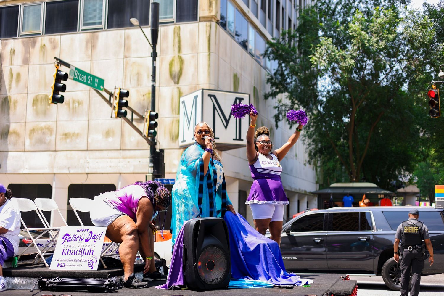 Performers in bright blue and purple outfits singing and dancing on an outdoor stage.