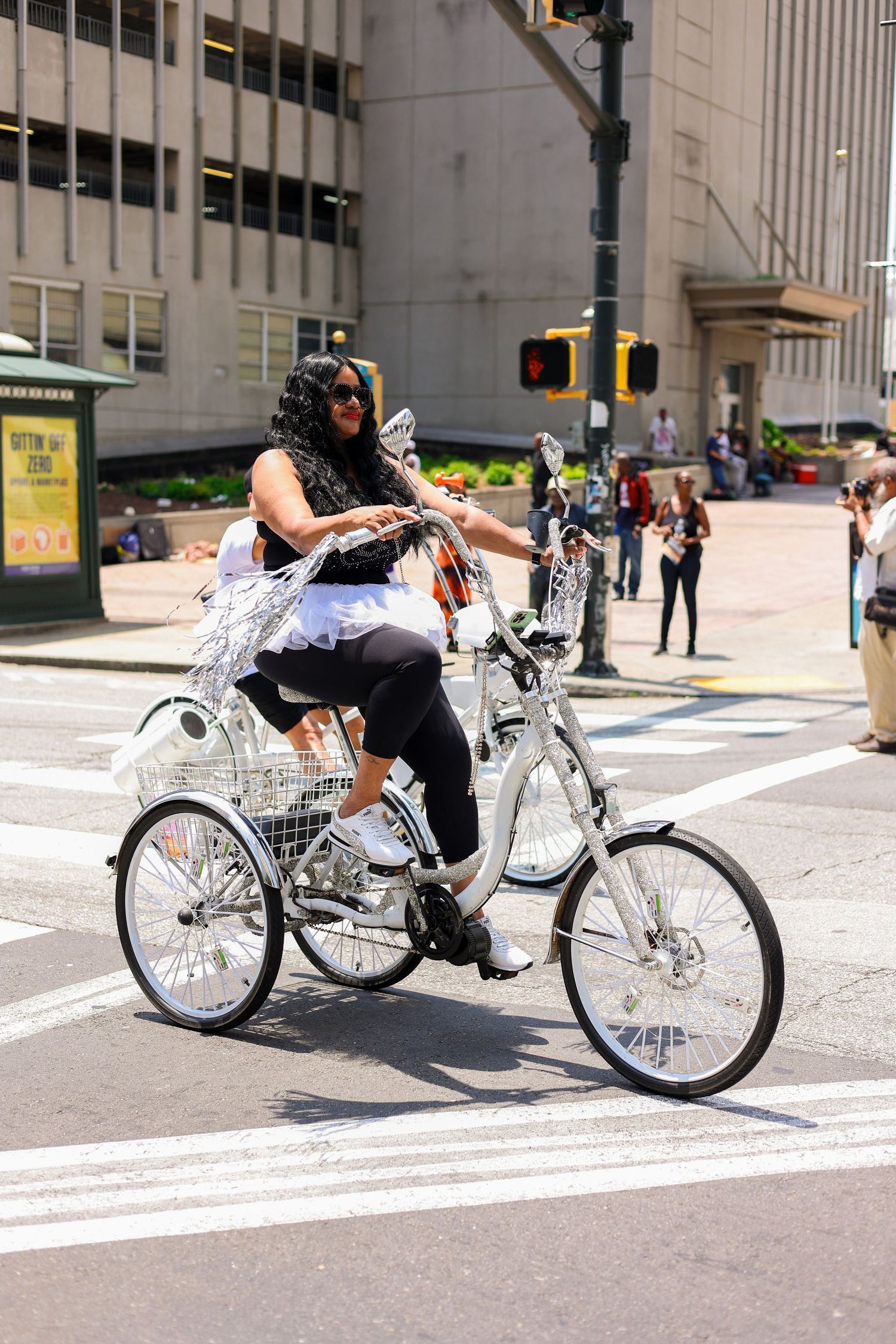 Person riding a custom three-wheeled bicycle through a downtown intersection.