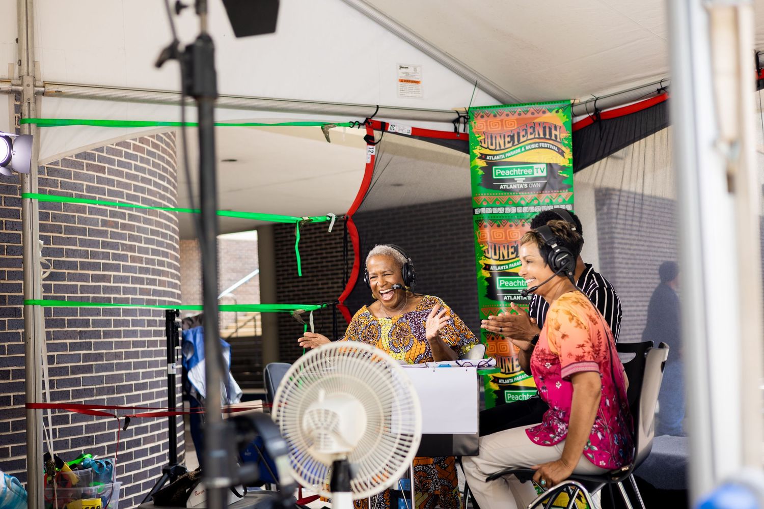 Musicians performing under a tent with audio equipment and fans.