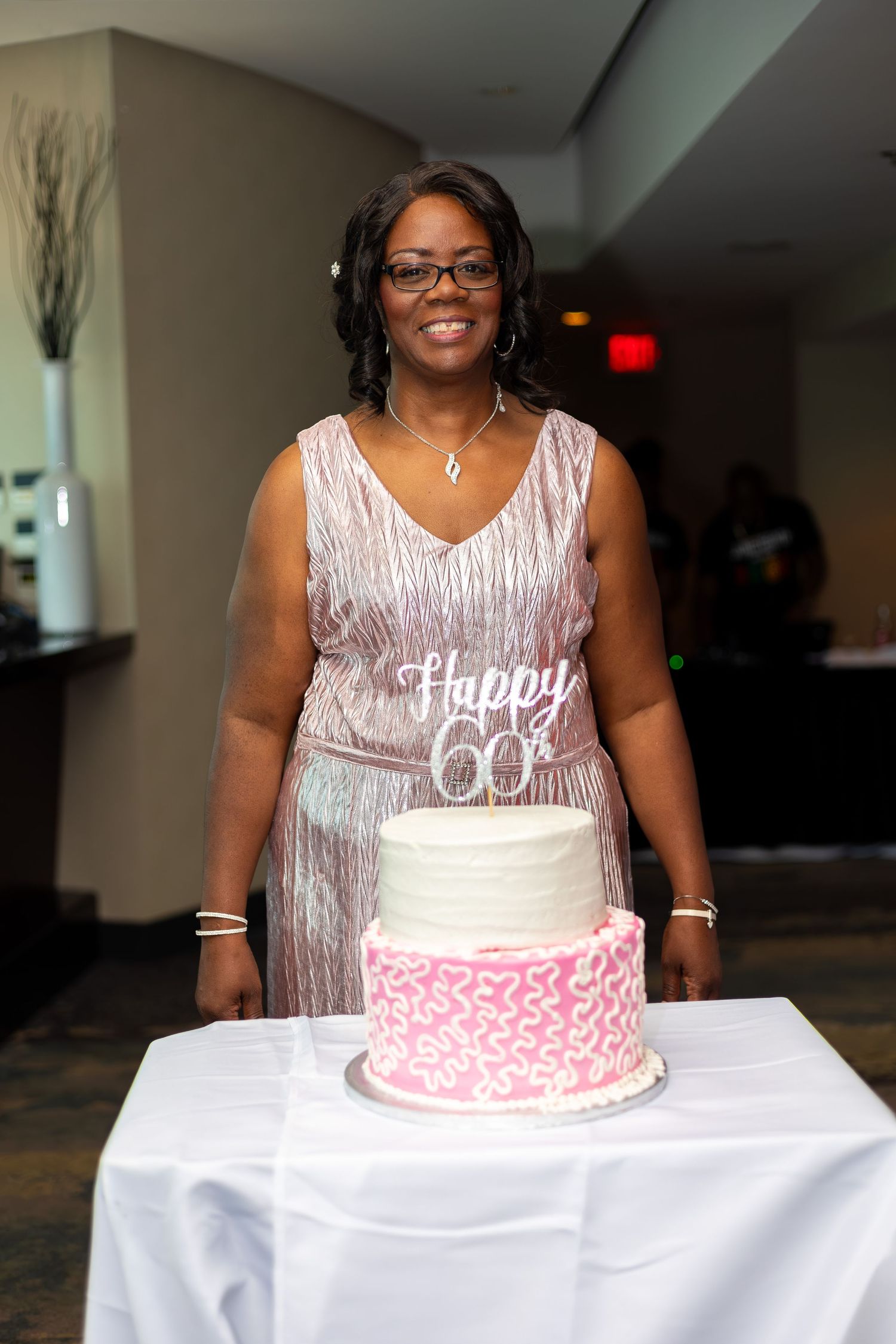 Celebrant in sparkly dress poses with 60th birthday cake at party.