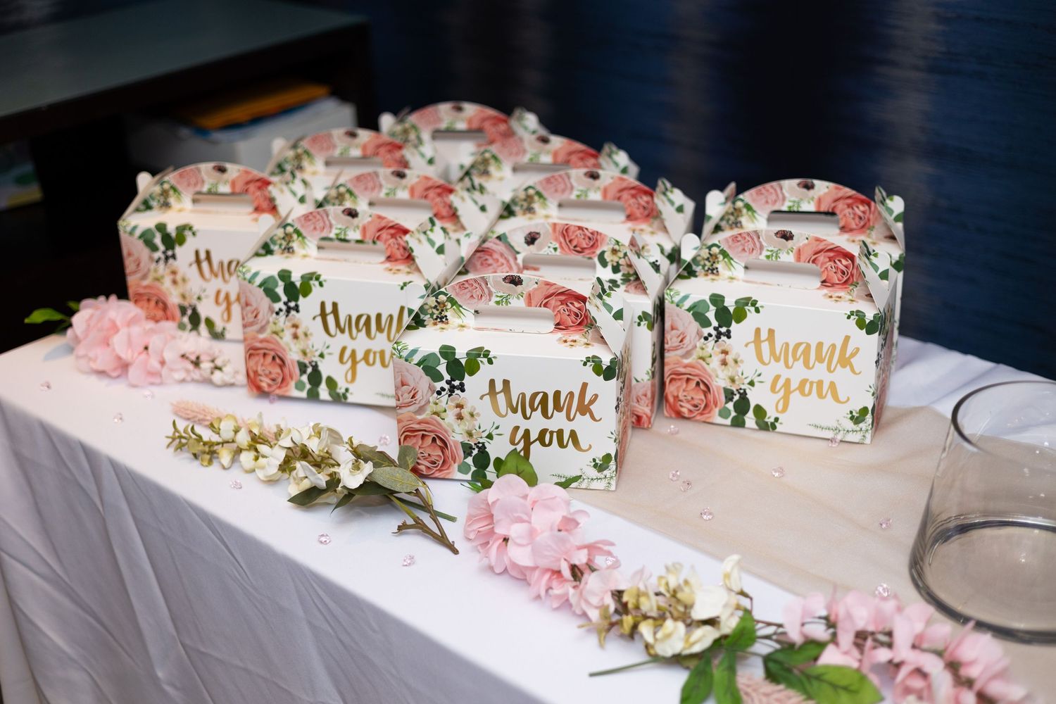 Beautifully decorated favor boxes with floral accents arranged on white tablecloth.