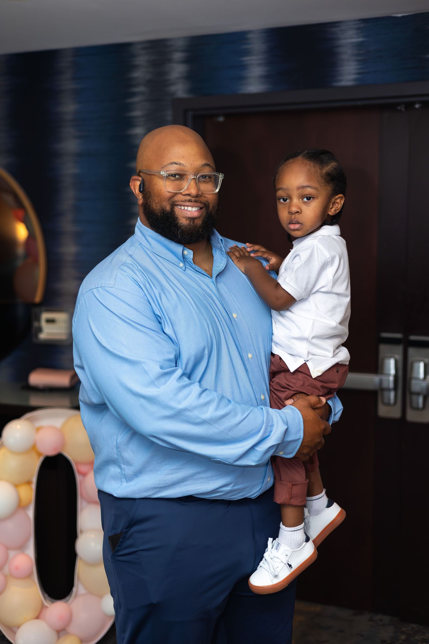 A tender family moment captured indoors with decorative balloons in background.