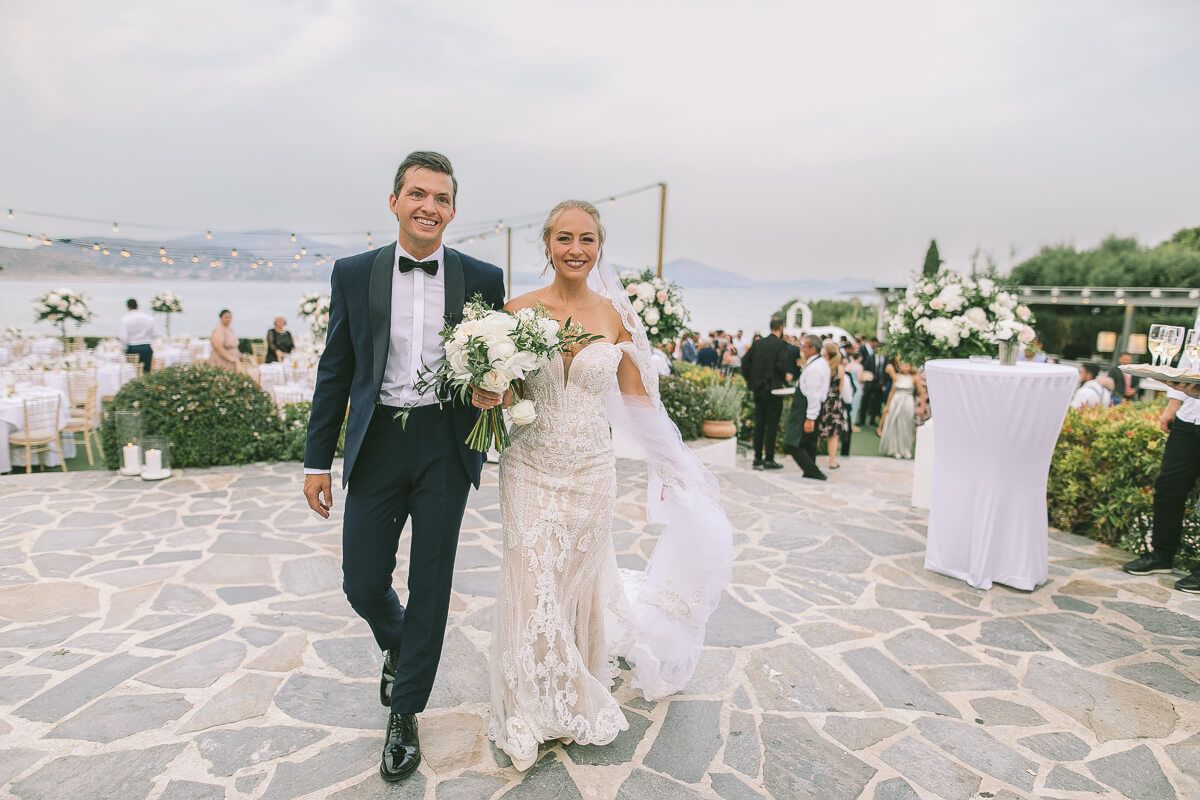 A bride and groom walk together on a stone patio at an outdoor wedding on Athens island riviera
