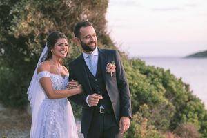 A couple in wedding attire embrace on a coastal cliff overlooking the ocean at sunset by GeorgeNafpliotis.com