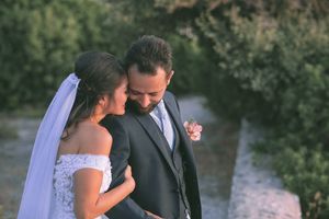 A couple in wedding attire embrace on a coastal cliff overlooking the ocean at sunset by GeorgeNafpliotis.com