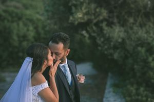 A couple in wedding attire embrace on a coastal cliff overlooking the ocean at sunset by GeorgeNafpliotis.com