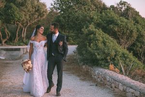 A couple in wedding attire embrace on a coastal cliff overlooking the ocean at sunset by GeorgeNafpliotis.com