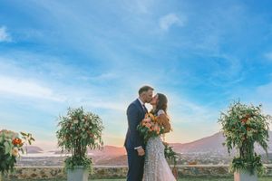 A couple shares a tender moment during their desert wedding ceremony at sunset framed by floral archways captured by GeorgeNafpliotis.com