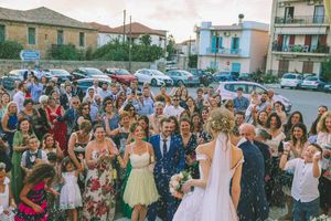 Crowd of wedding guests celebrating outdoors in a parking lot while throwing confetti on a sunny day in Greece.www.georgenafpliotis.com