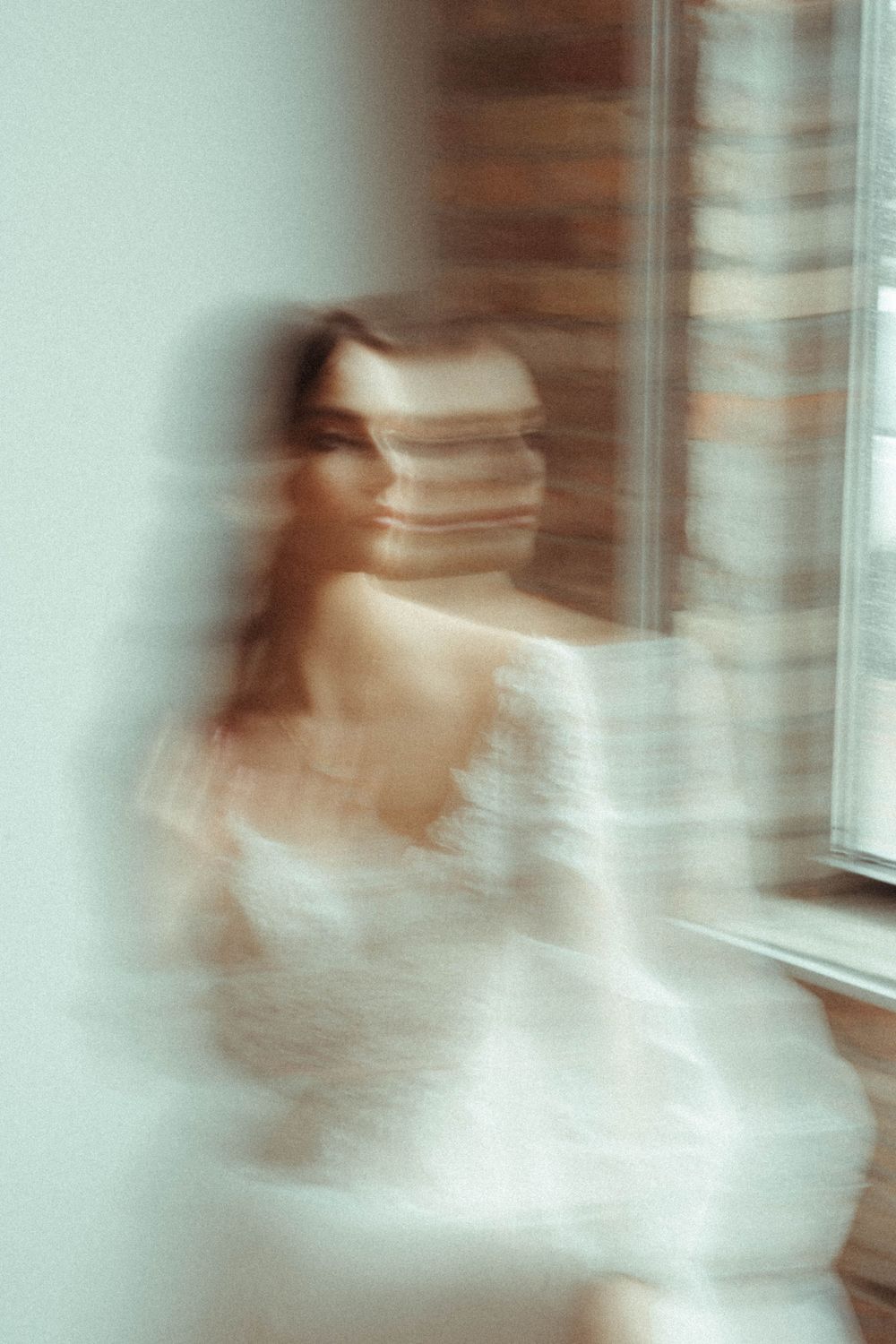 Artistic blurred motion photograph of a bride in white by a window.