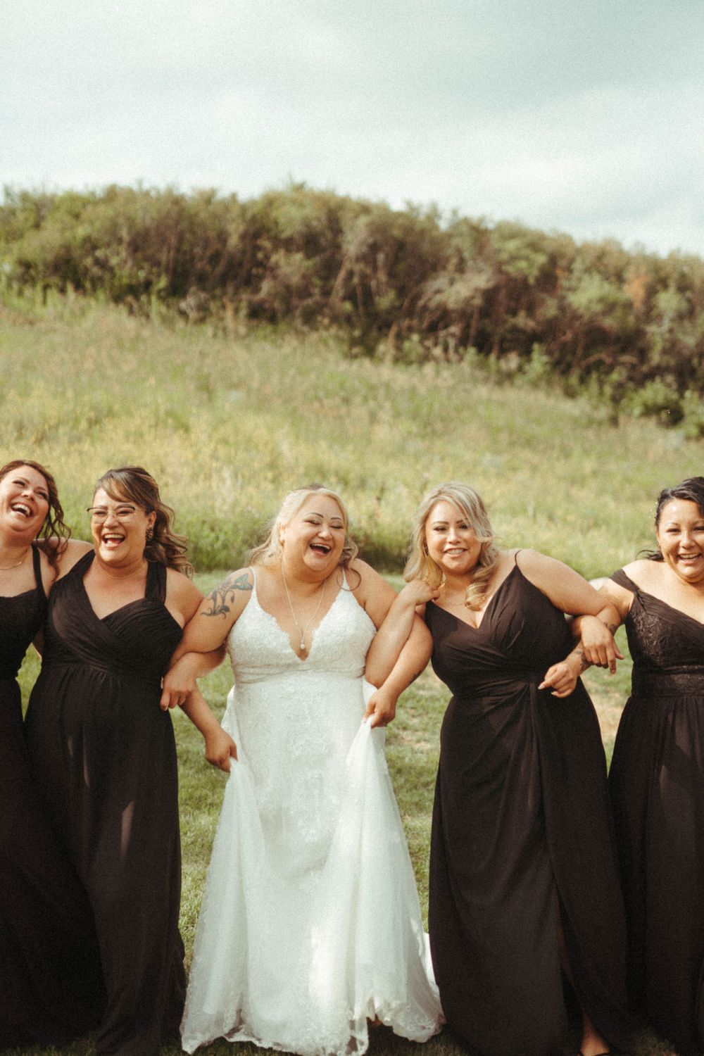 Wedding party in coordinated black and white dresses poses together on a grassy hillside.