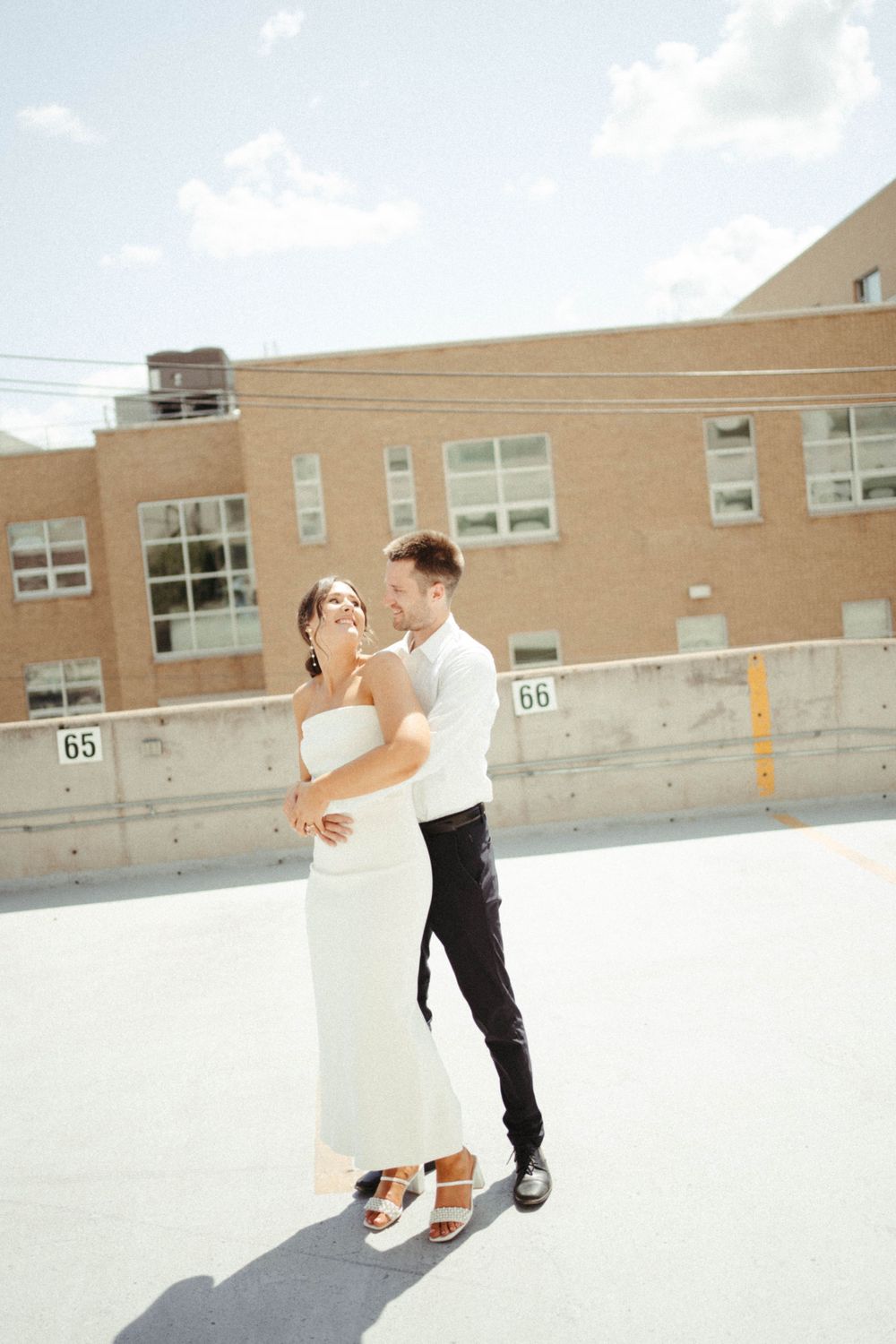 Sun-lit portrait of couple in wedding attire dancing on rooftop.