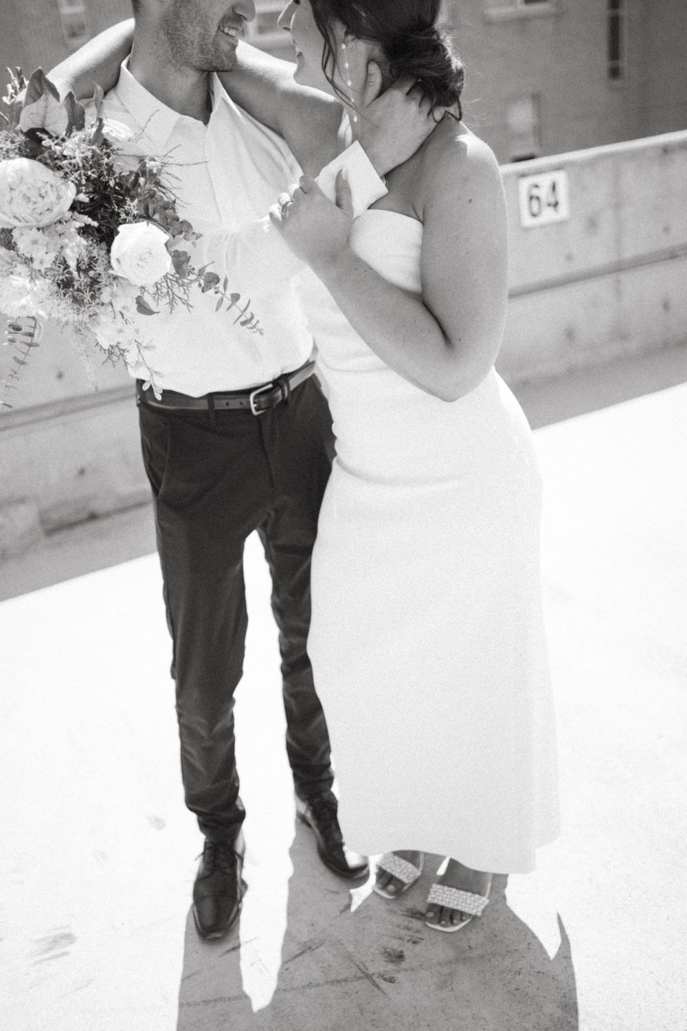 Black and white intimate moment between couple with bouquet on urban rooftop.