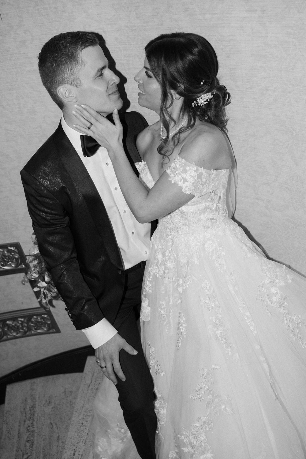 A romantic black and white portrait of newlyweds sharing an intimate moment in formal attire.
