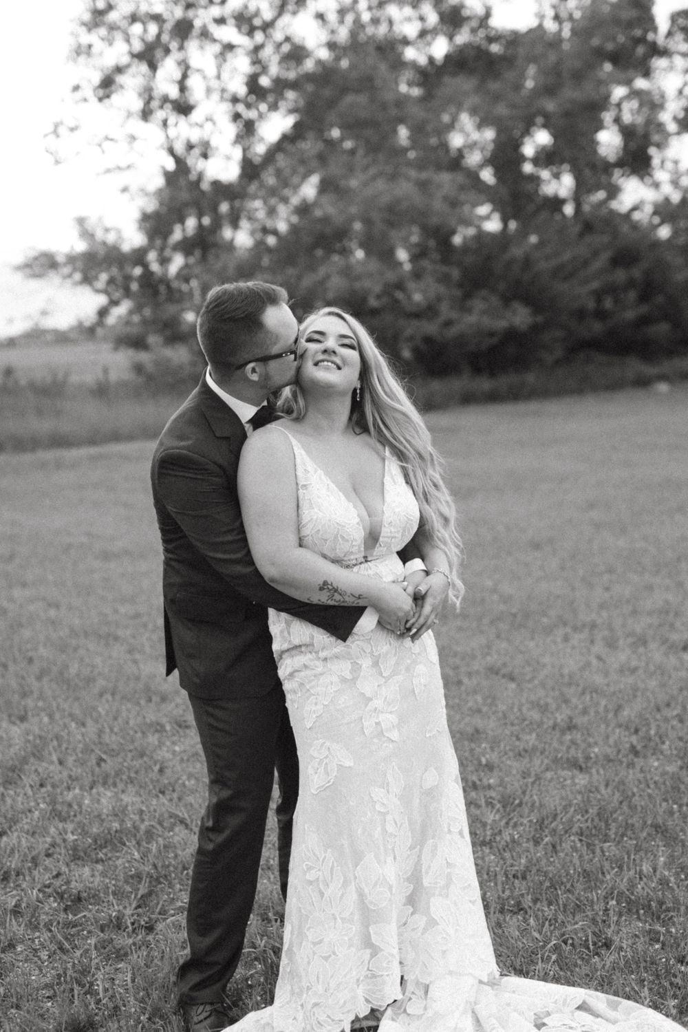 A joyful outdoor wedding portrait of a couple laughing together in a grassy field.