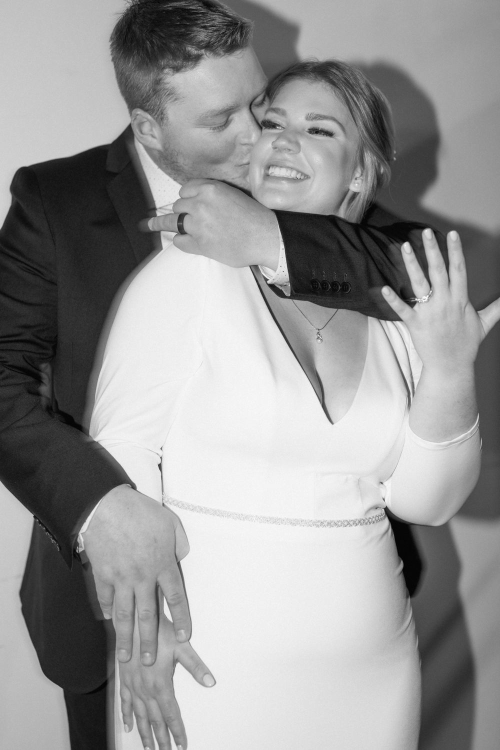 Black and white candid wedding photo captures playful embrace and laughter.