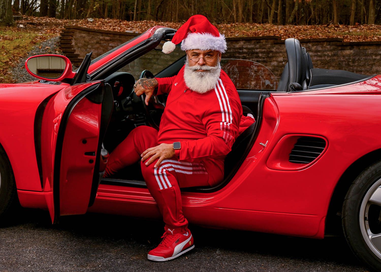 Person in red tracksuit and Santa hat sitting in red sports car.