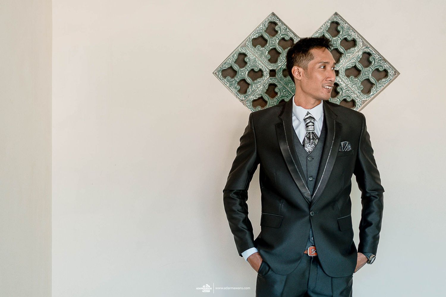 A person in a tailored suit poses against a modern geometric wall design.