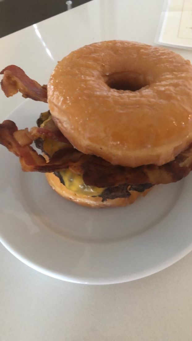Close-up of a glazed donut burger with bacon and cheese on a white plate.