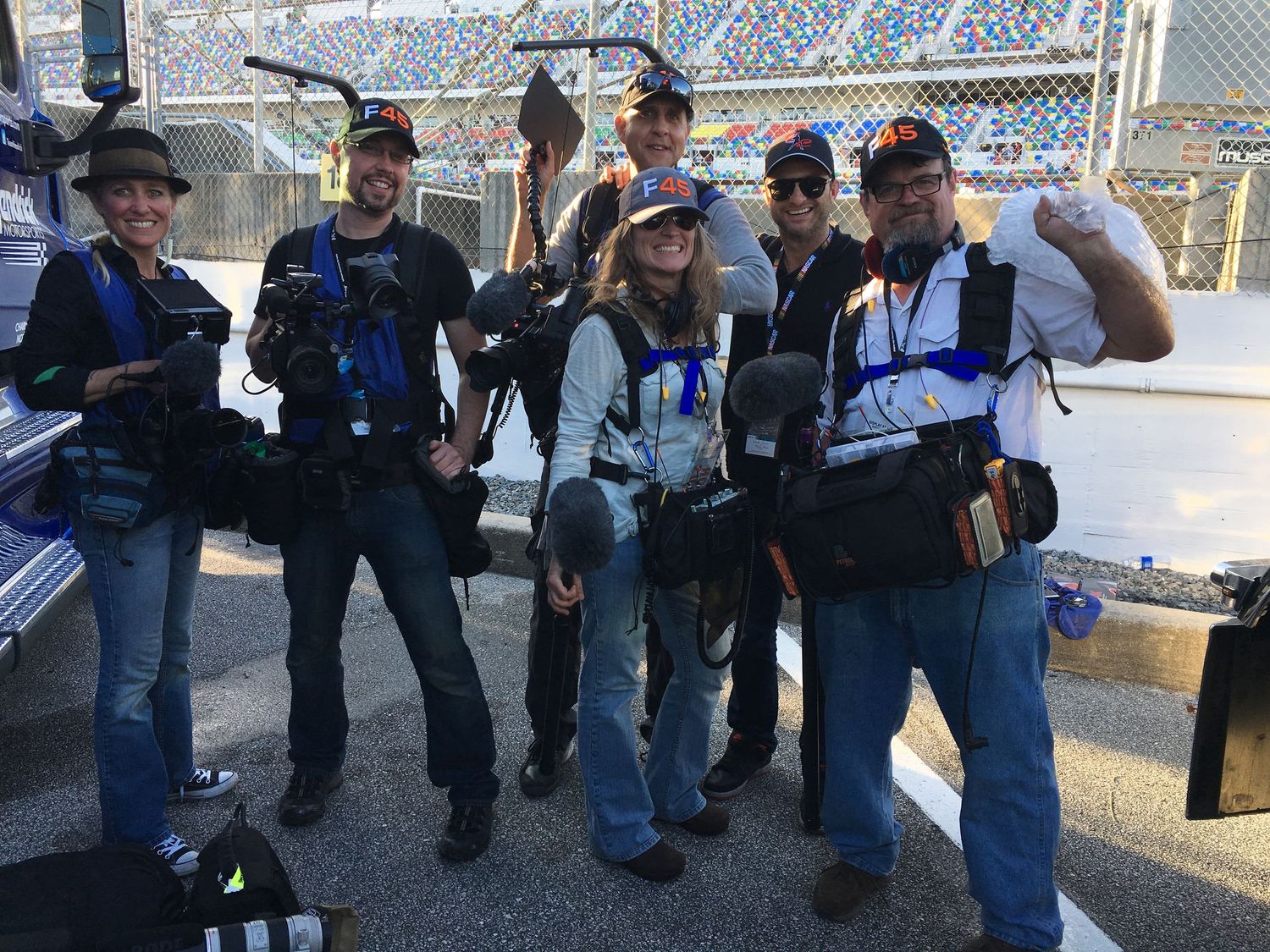 Group of camera operators and production crew posing with equipment at sports venue.