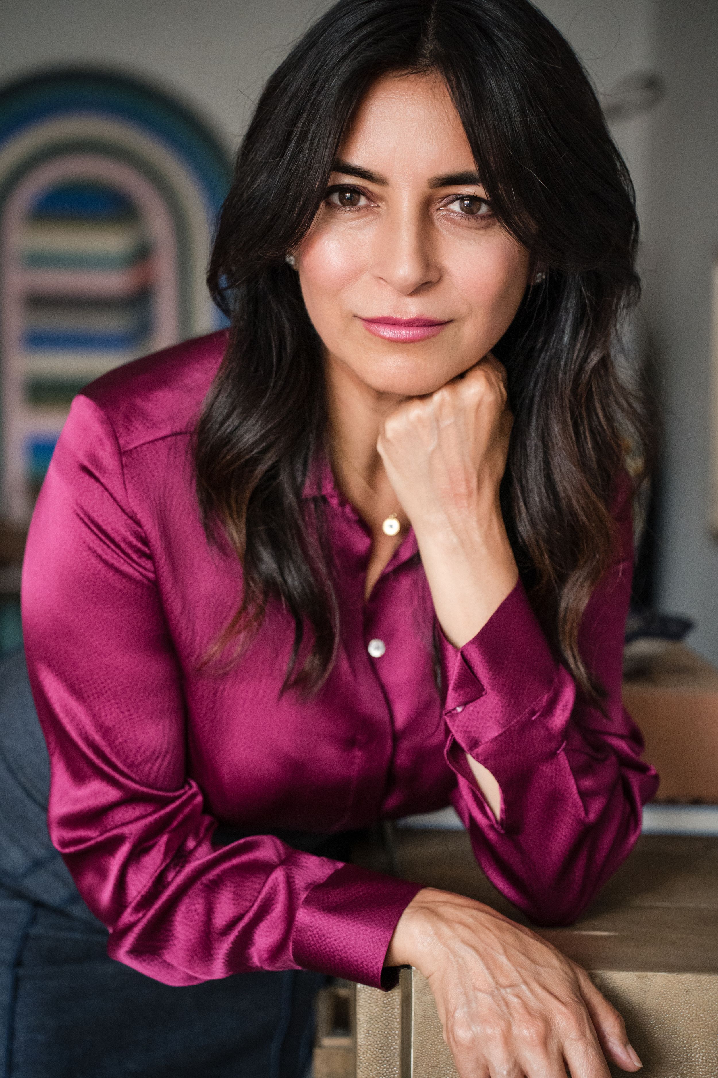 An elegant woman in a magenta silk blouse rests her chin on her hand thoughtfully.