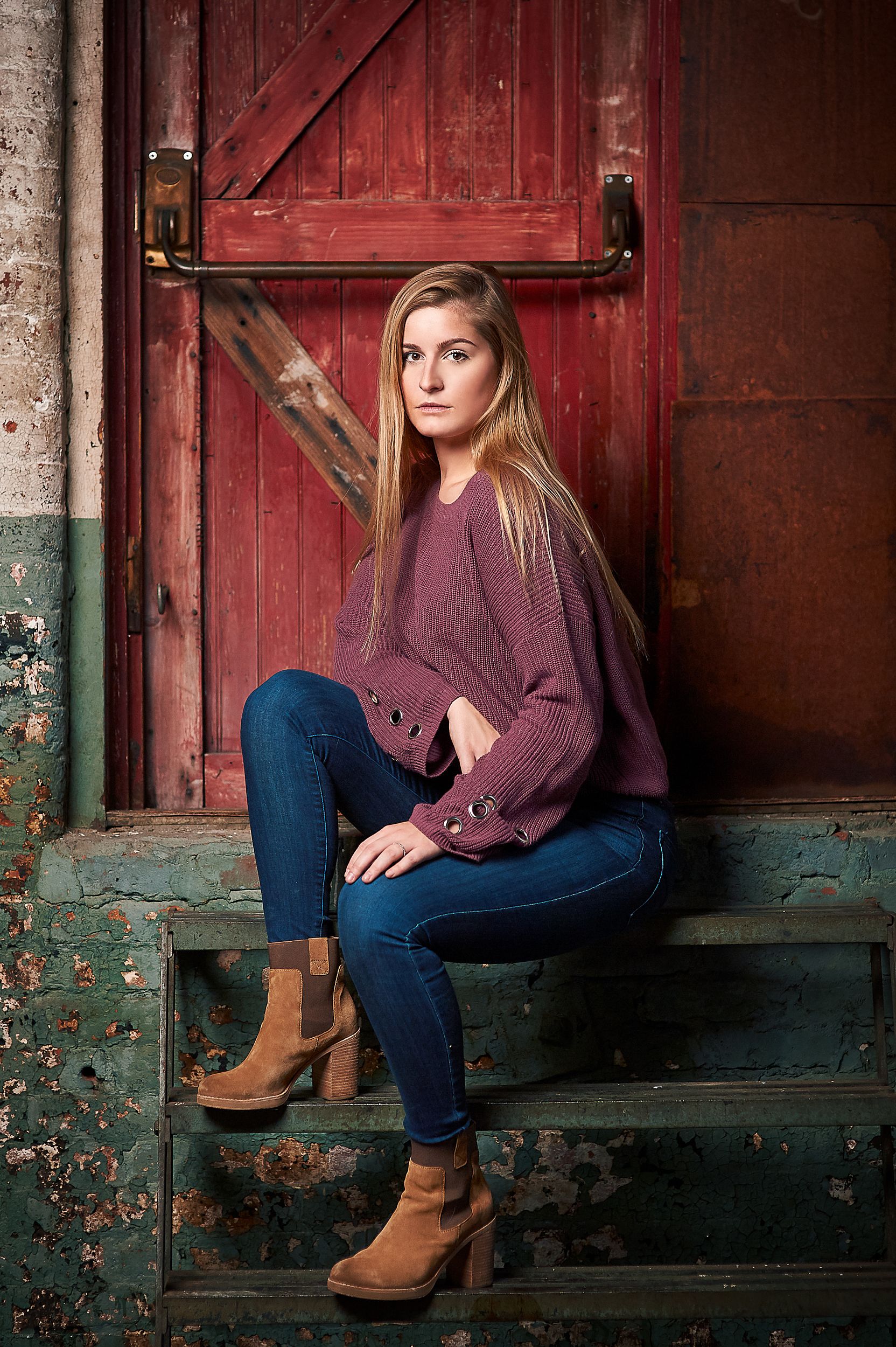 A young blonde woman in a purple sweater and jeans sits on rustic barn steps.