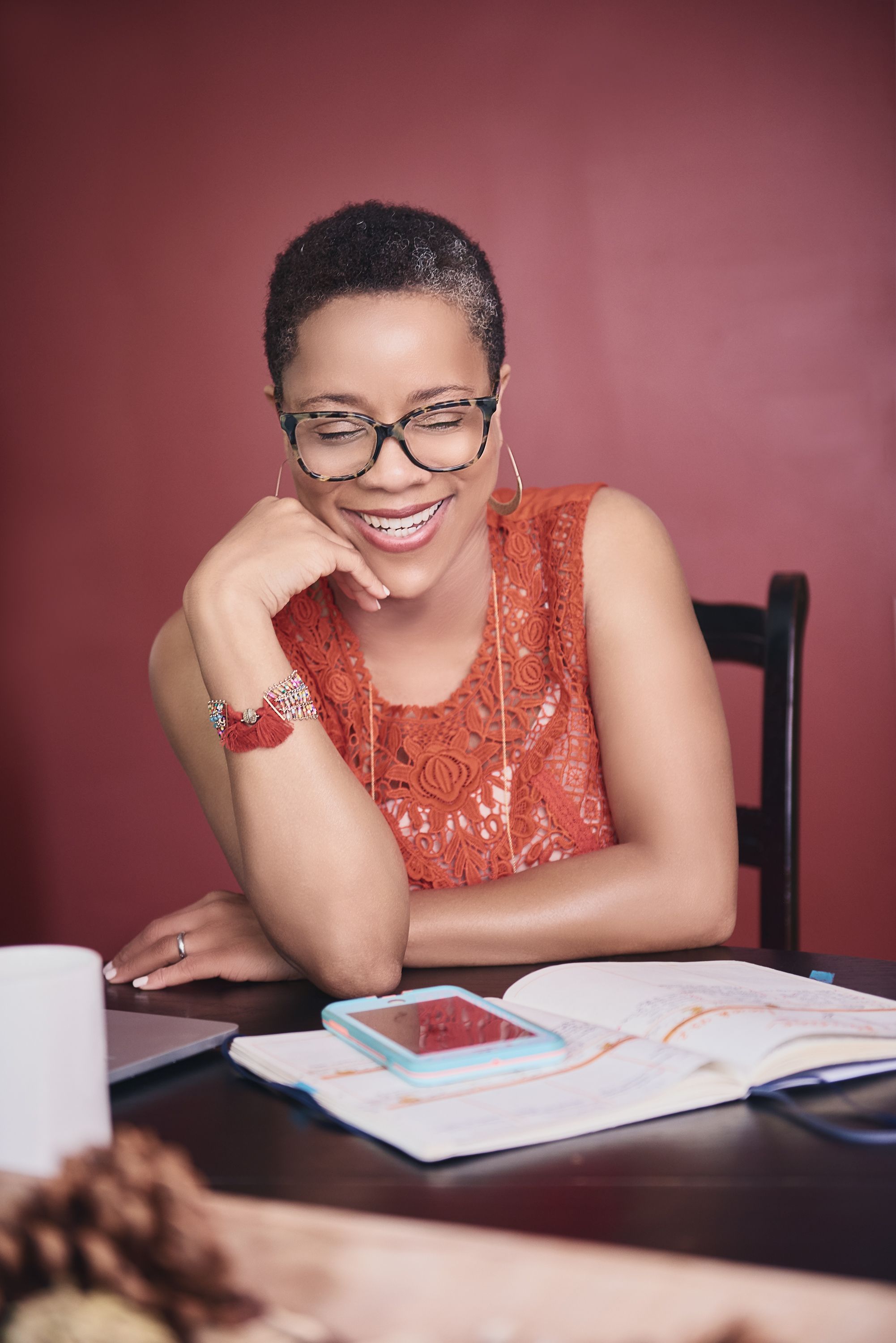 A cheerful woman with short hair and glasses smiles while studying at a desk.