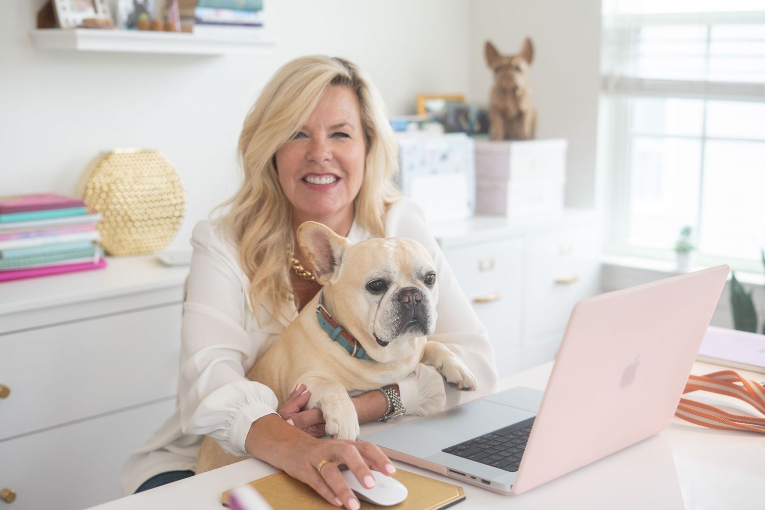 Woman working from home office with laptop while cuddling French Bulldog.