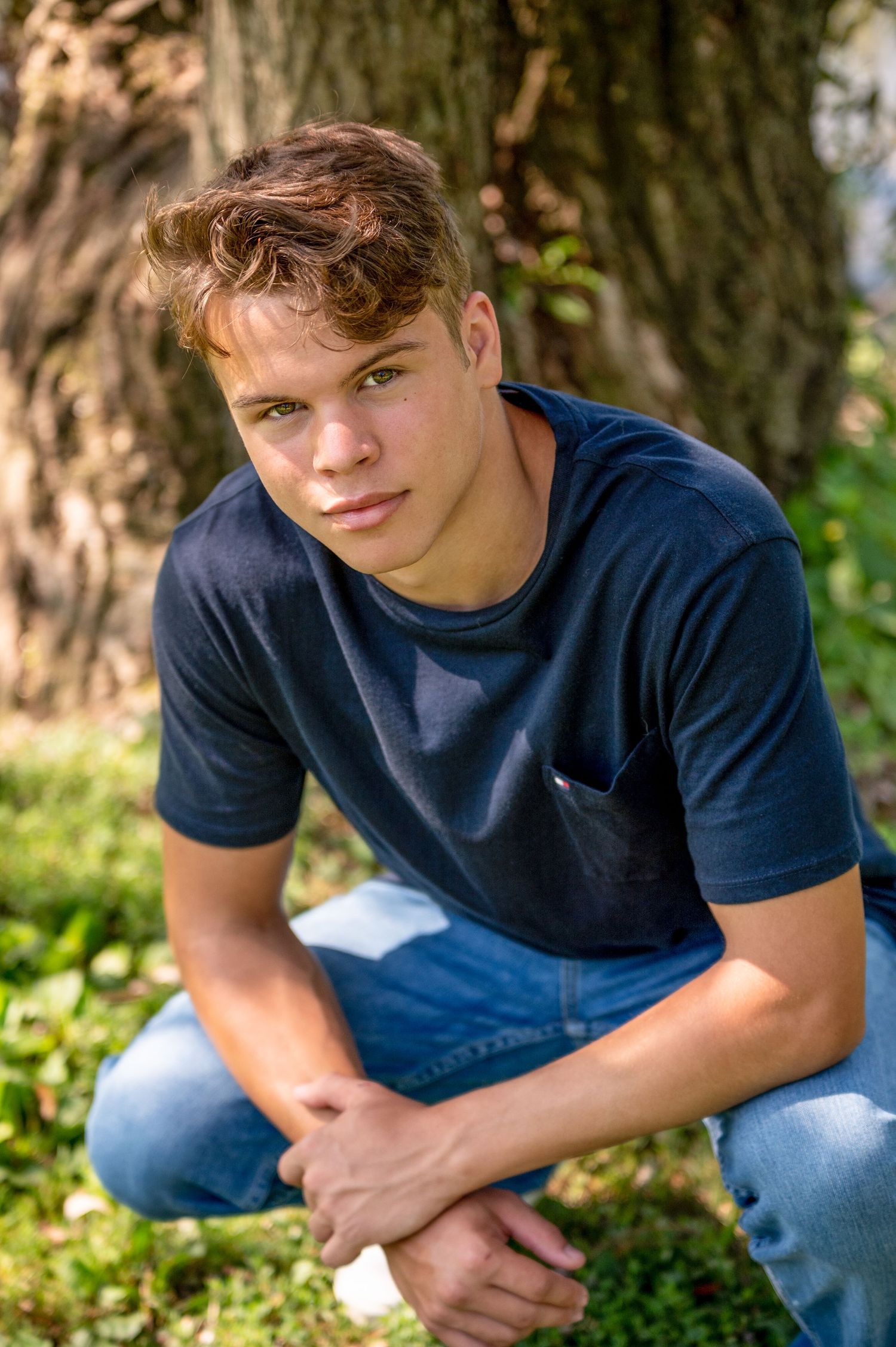 Casual outdoor portrait of young person in navy shirt against tree background.