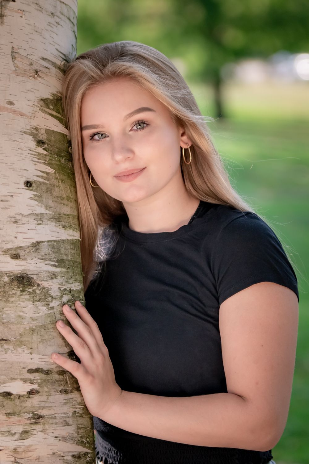 A portrait next to a birch tree trunk in a black t-shirt.