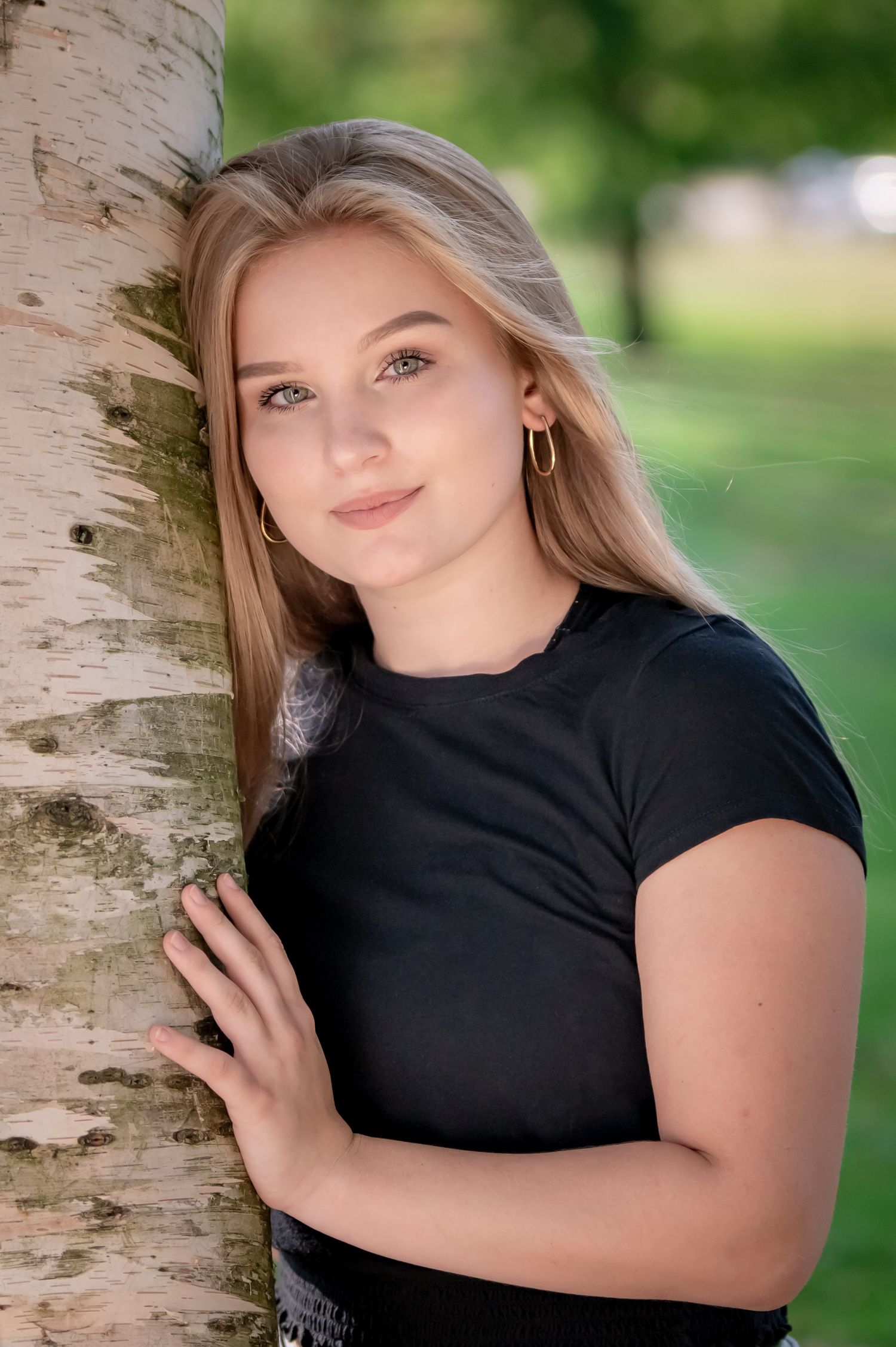 A portrait next to a birch tree trunk in a black t-shirt.